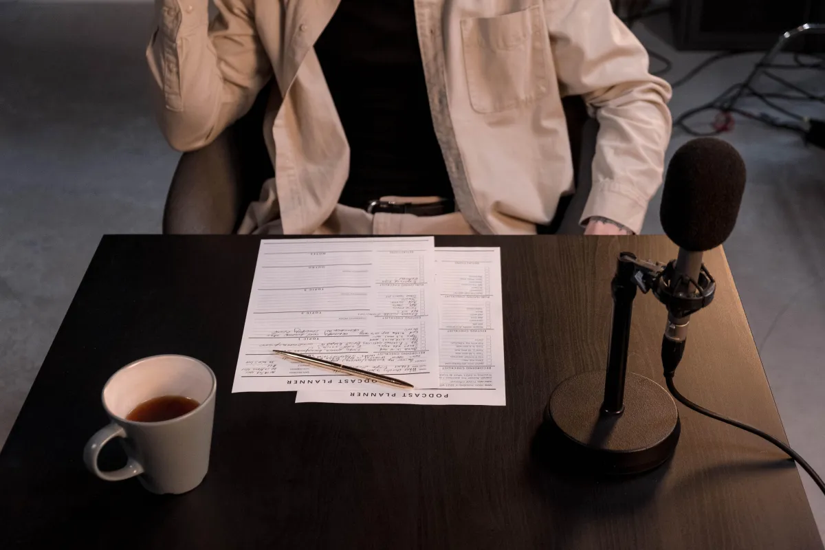 person sitting at desk with papers, pencil, coffee cup, and microphone on it