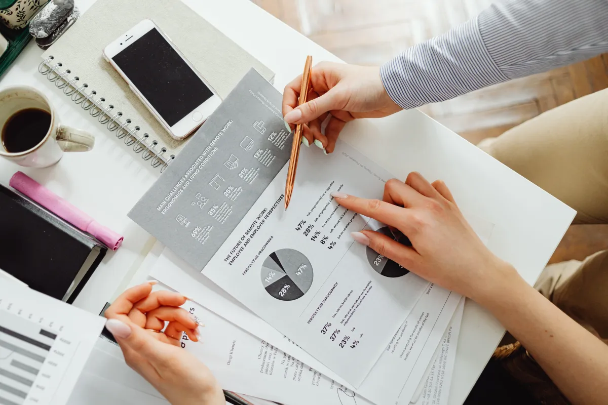 people pointing at graph sitting on desk with coffee and phones