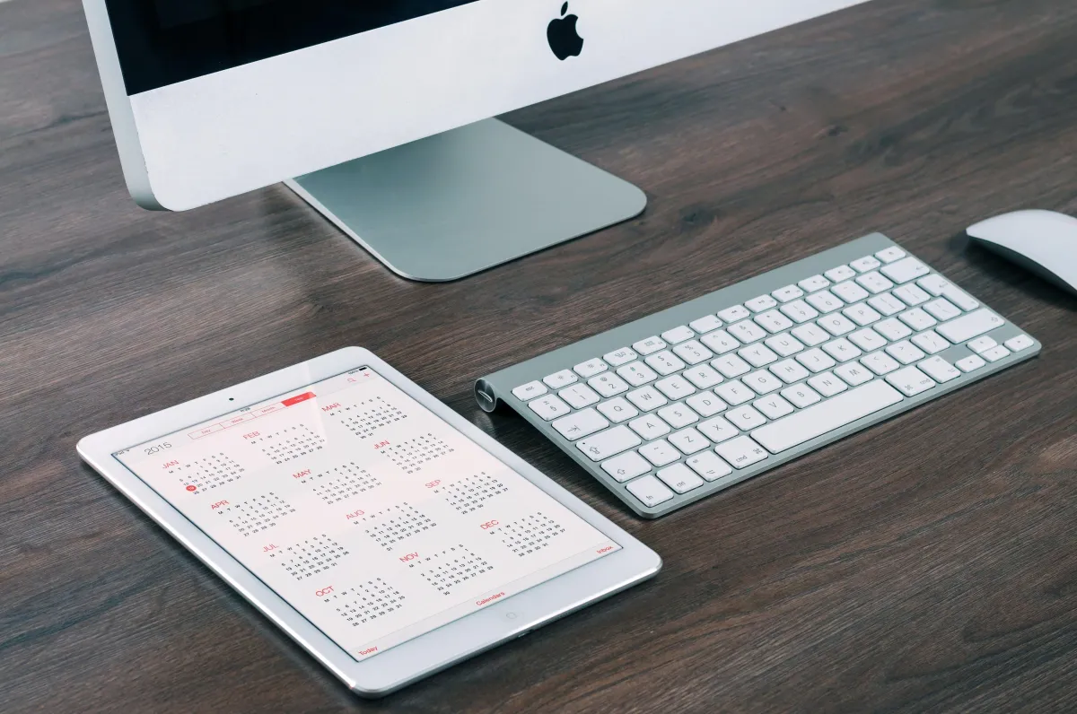 Digital calendar on an ipad next to a mac computer and keyboard all on a desk