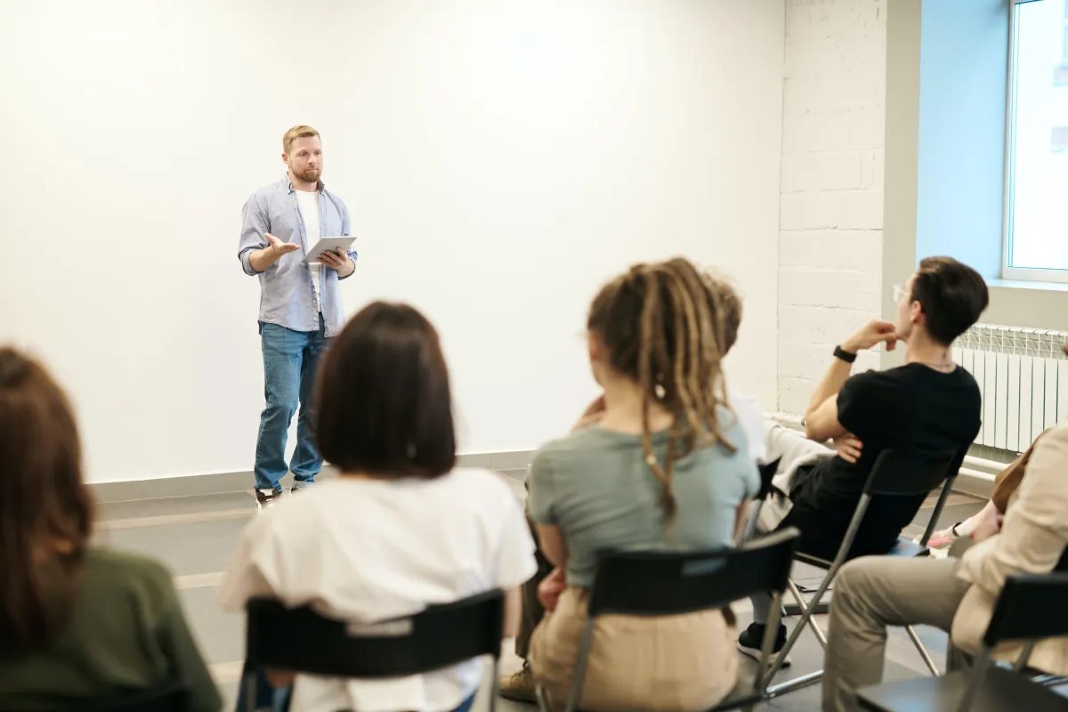 Man standing in front of a white wall presenting to a group of people