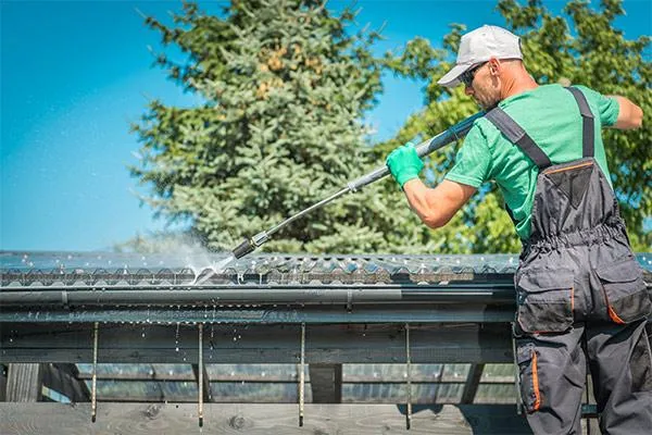 A roofer cleaning a roof gutter through power washing