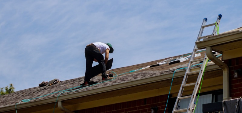 worker applies gray shingles to house roof
