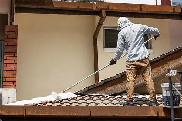 a roofer using a paint roller in painting a roofing tiles
