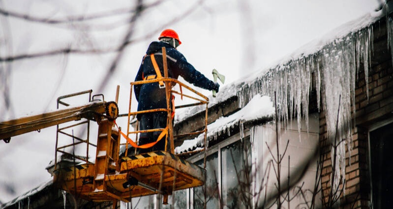 a worker performs roof maintenance, clearing ice flakes from the roof's surface to prevent damage