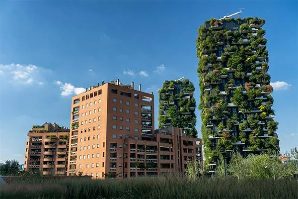 The Bosco Verticale in Milan, Italy, showcasing two iconic residential towers covered with vertical gardens, surrounded by traditional buildings and greenery under a clear blue sky