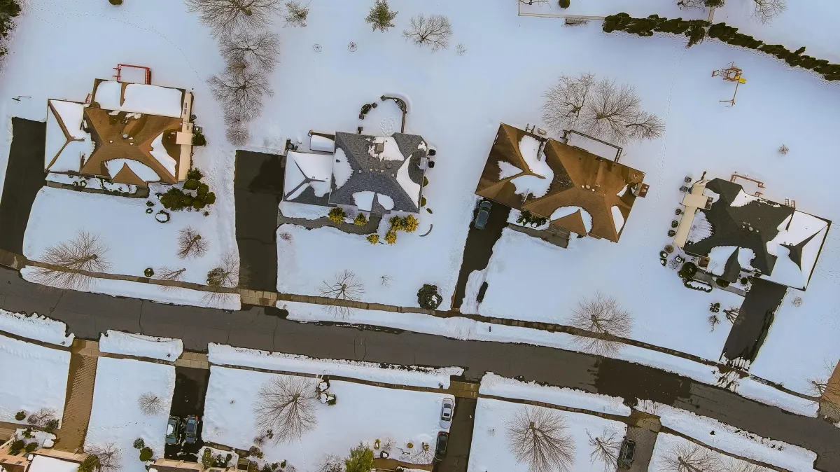 Aerial view of suburban houses with snow-covered roofs in winter, highlighting the impact of cold weather on roofing and insulation efficiency.