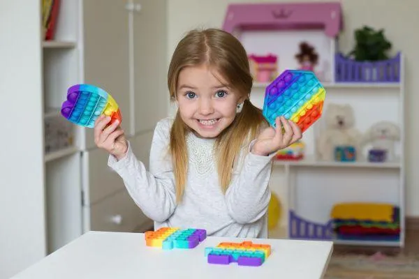 Image of young girl with blonde pigtails, grinning as she holds up colourful sensory toys
