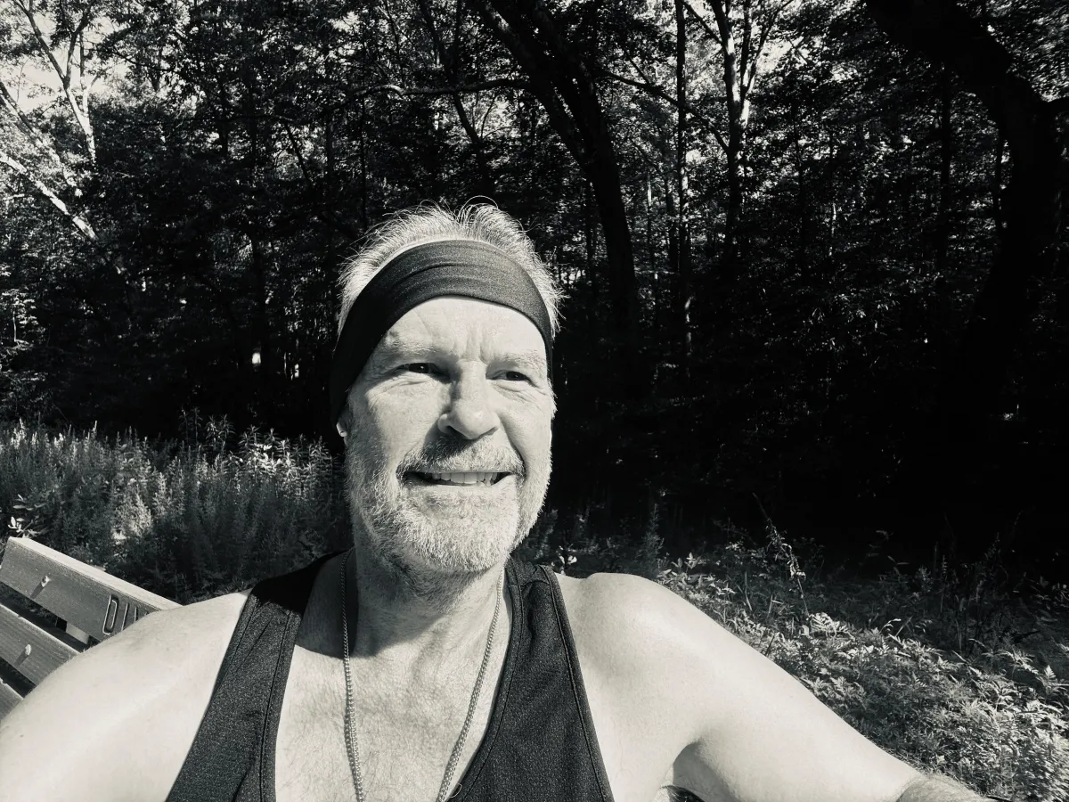 Jeff Simpson sitting on a bench in the woods, sunlight catching his face as he looks ahead, thoughtful but grounded—embodying peace after a long internal struggle.