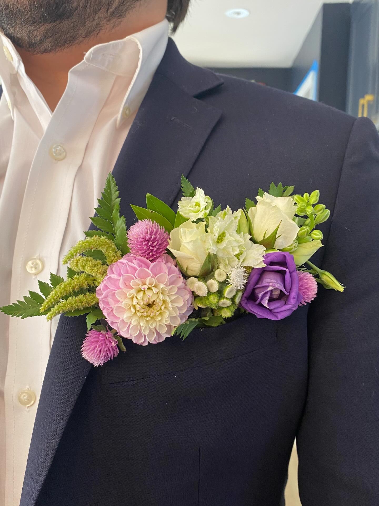 Seasonal wedding boutonniere with dahlias, lisianthus, and textured greenery styled on a groom’s navy suit