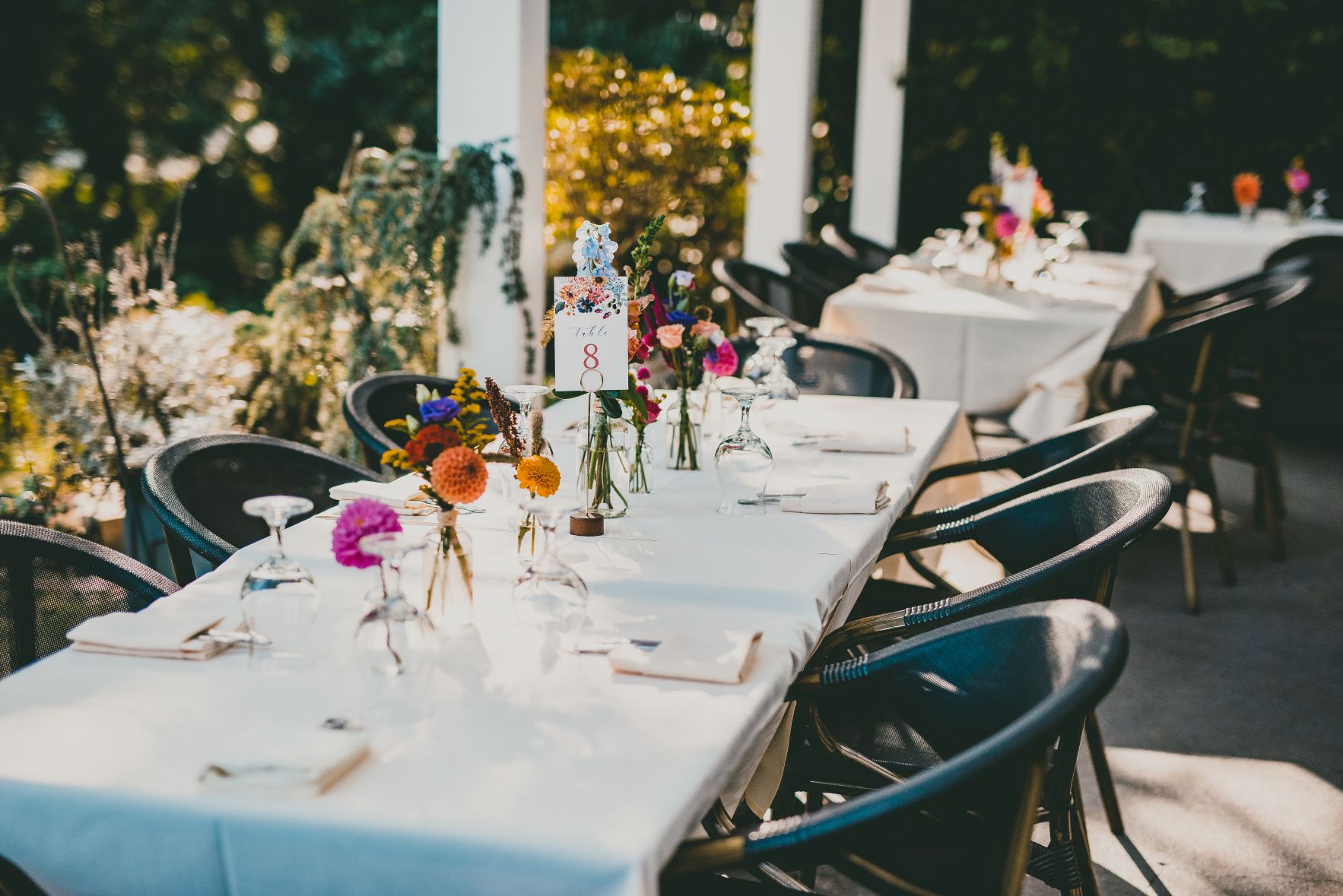 Colorful fall flowers in clear medicine bottles collective centerpieces on dining tables with white linens