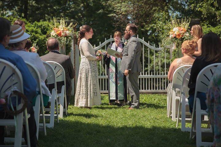 Outdoor garden wedding ceremony with tall altar arrangements in creamy white, orange, peach, and pink.