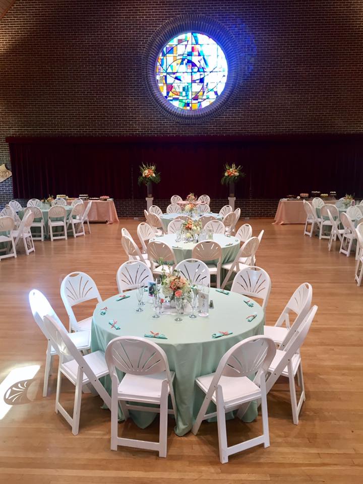 wedding reception room with large round tables with mint green linens and peachy, pink, and orange floral centerpieces with two large altar arrangements around the sweetheart table.