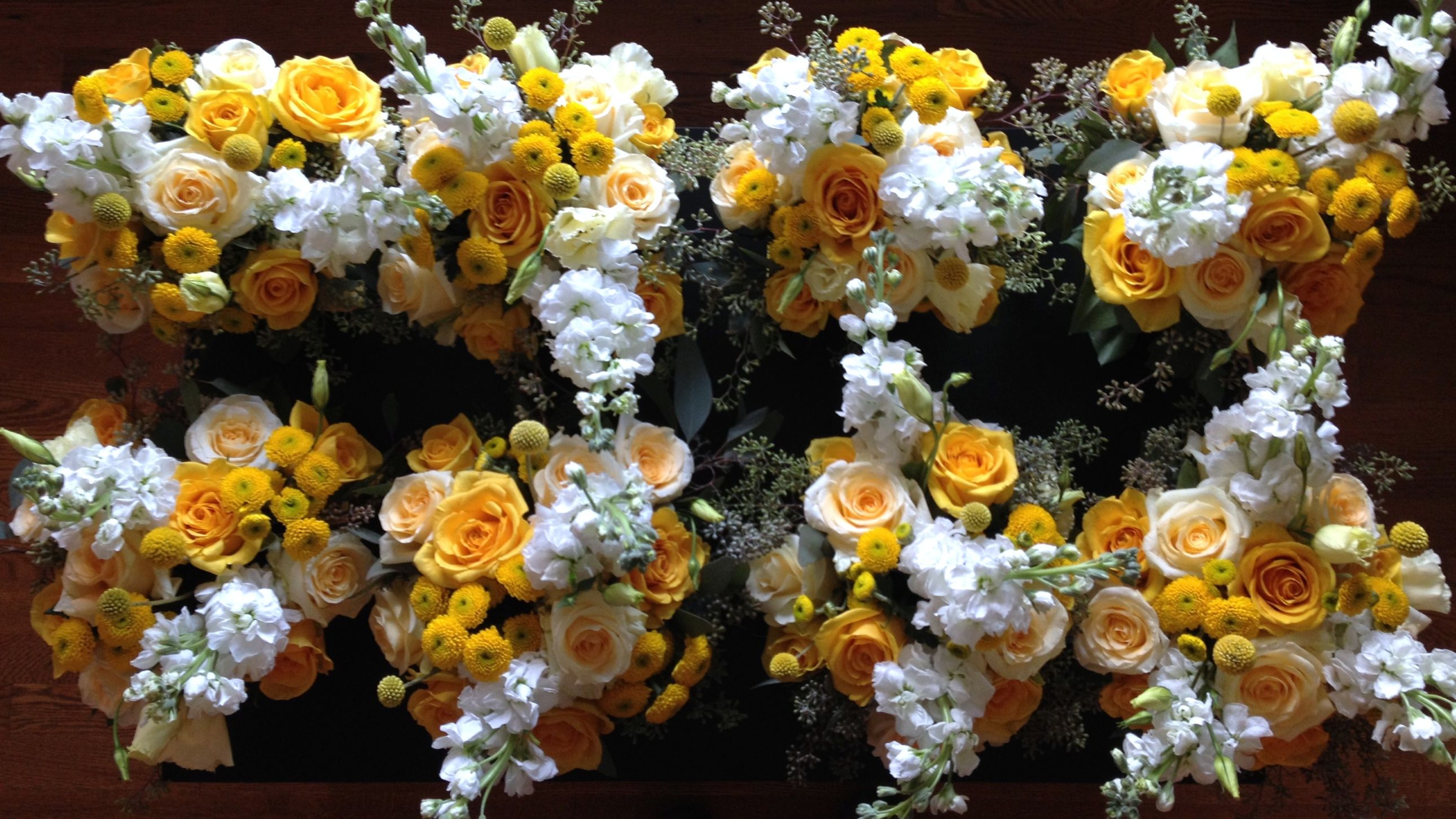 Yellow and white square floral centerpieces with yellow, cream roses, white stock, yellow button mum, craspedia balls