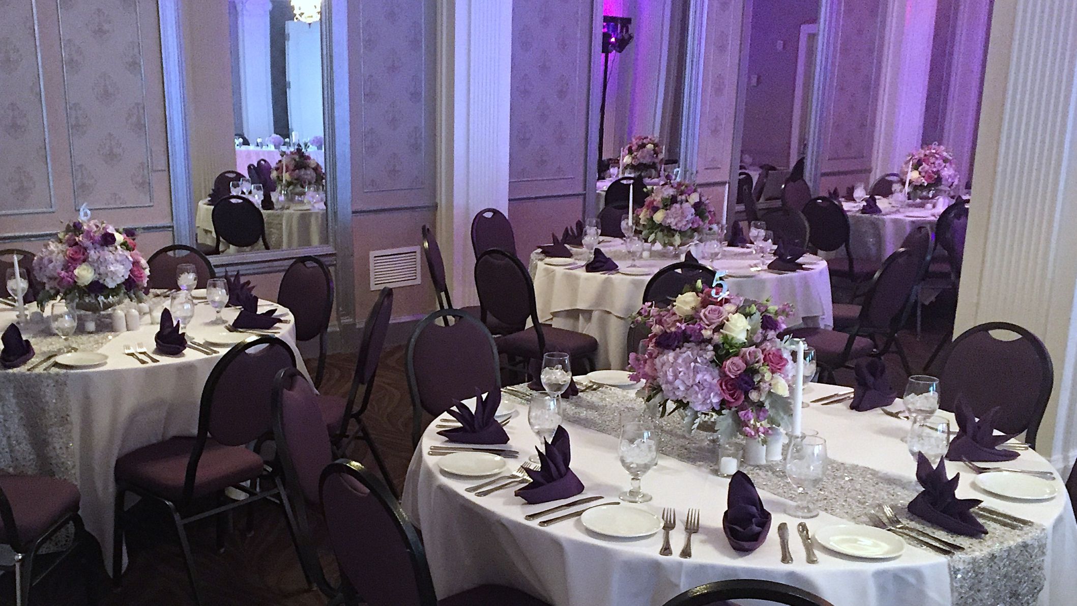 Reception dining tables with large floral centerpieces in shades of purple, cream, and lavender