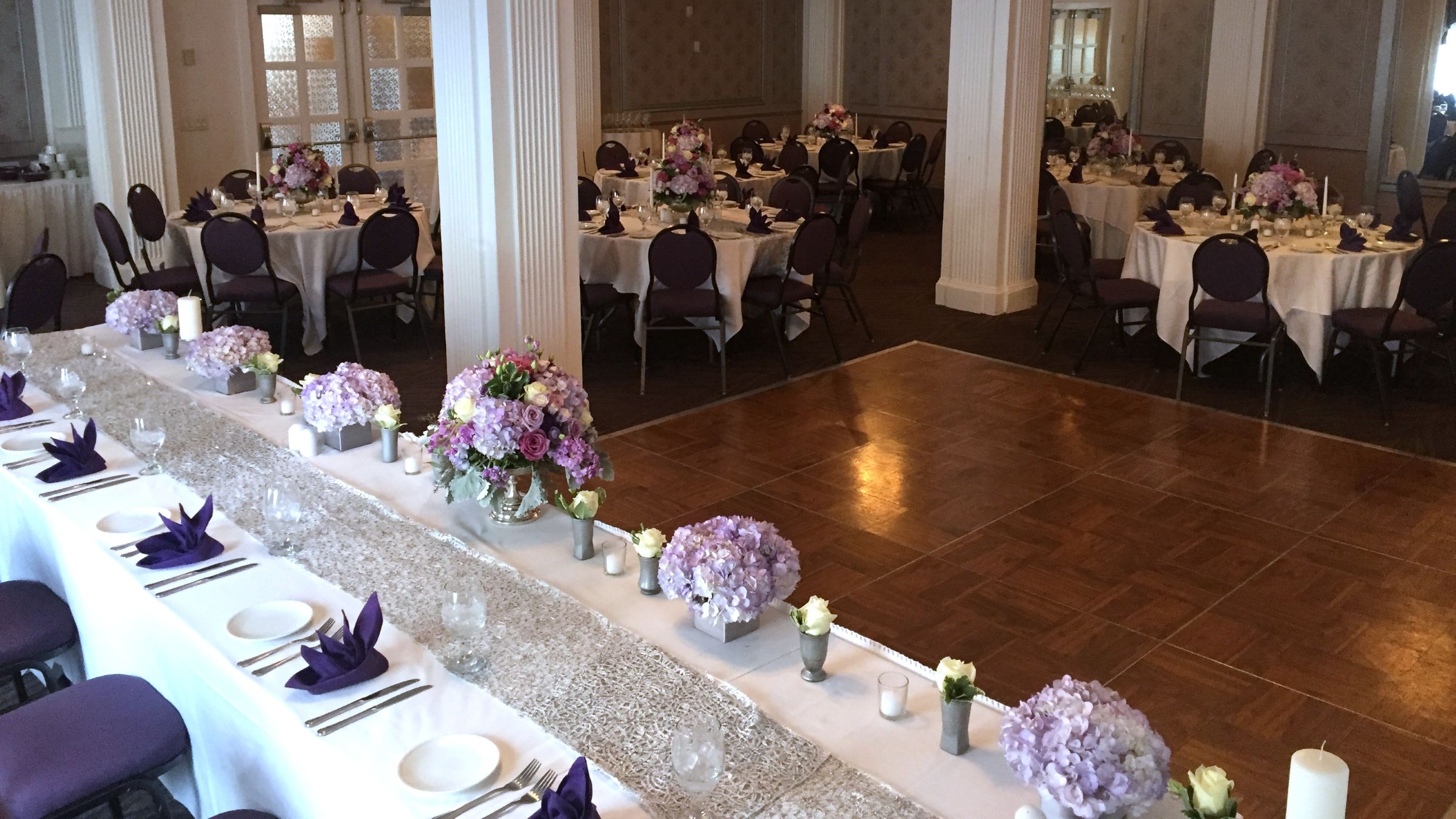 Wedding reception head table and dining tables with flowers in shades of purple, lavender, and white.