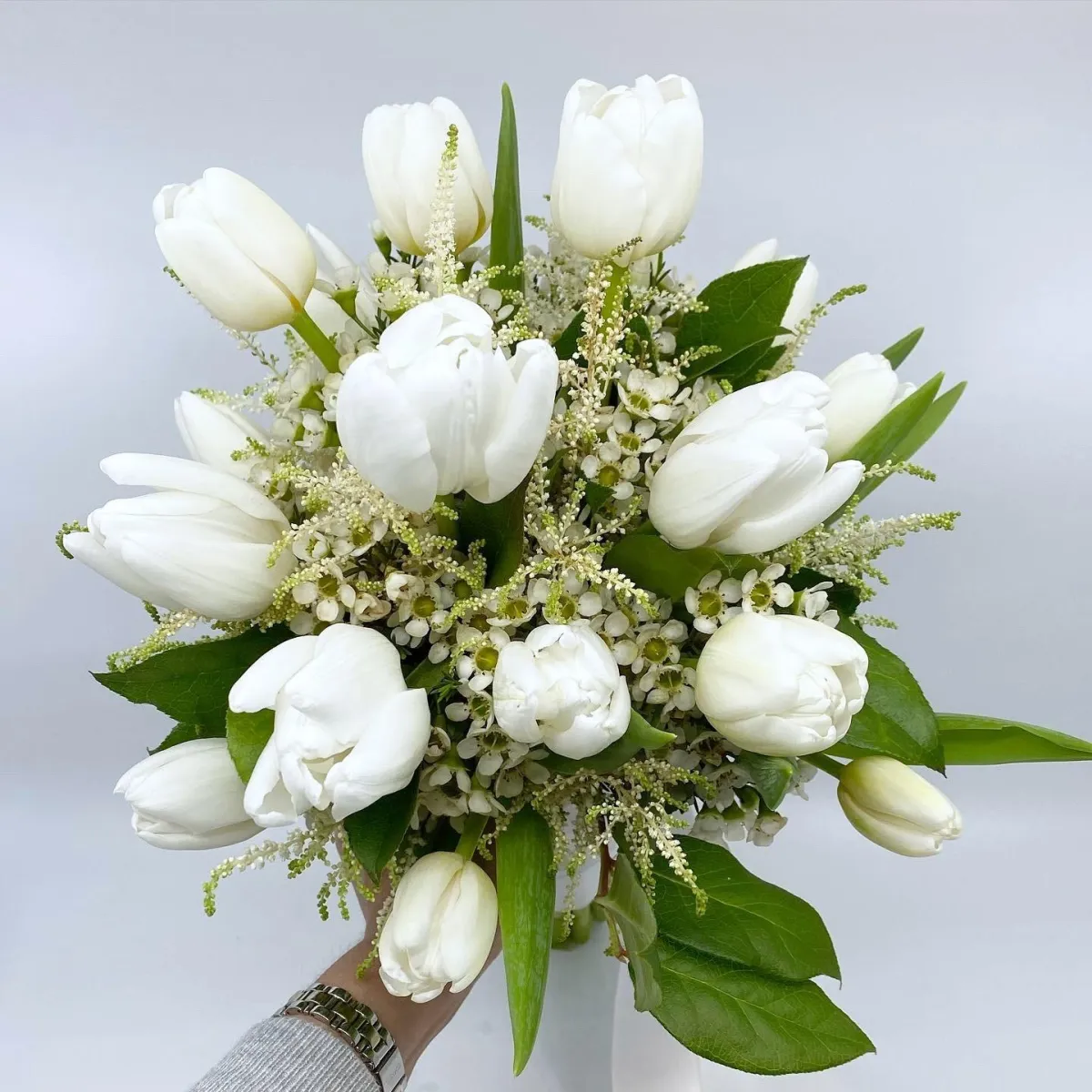 A bridal bouquet of white tulips, waxflower, and astilbe, and lemon leaf.