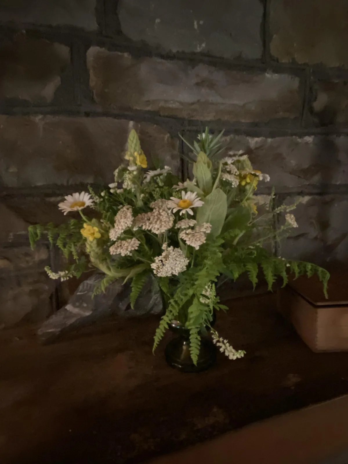 A small accent floral arrangement on a fireplace mantel of July foraged wildflowers and foliage in white and yellow with natural greens.