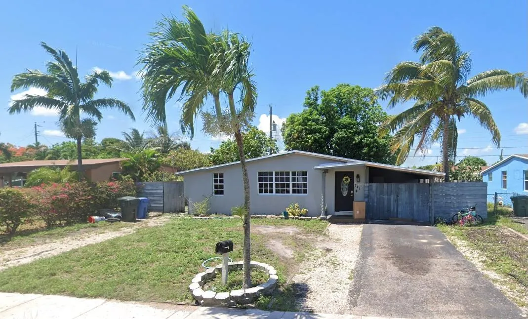 Front view of 741 NE 58th St, Oakland Park, FL — a single-story home with a fenced yard, carport, and mature landscaping in Collier Estates.