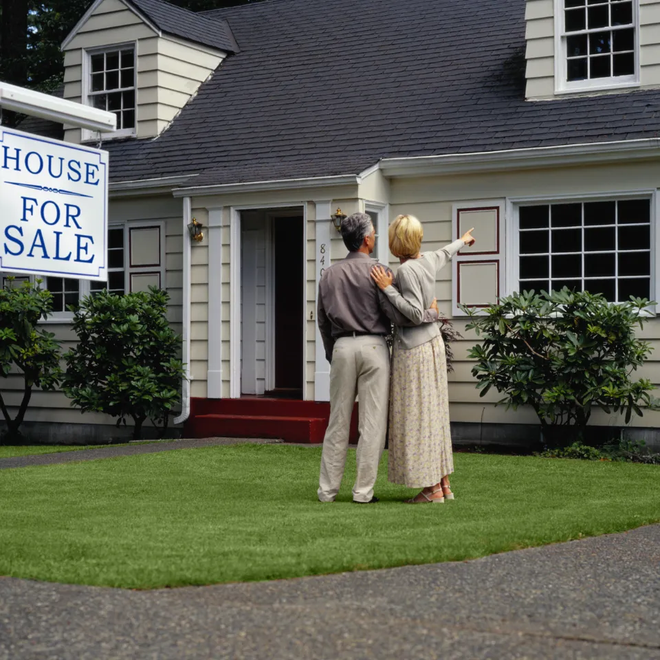 Couple touring a home with holiday lights and a “For Sale” sign out front.