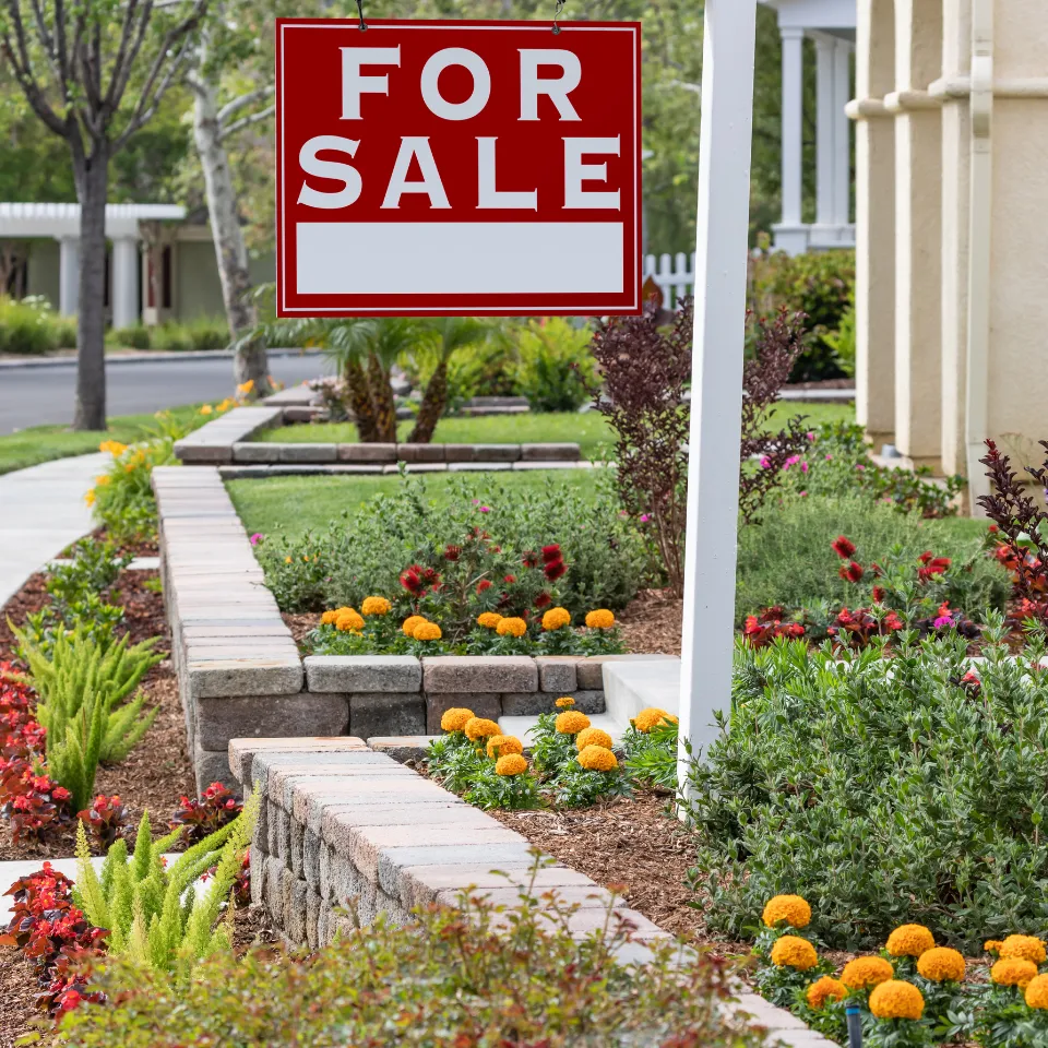 Beautiful spring home with fresh landscaping and a “For Sale” sign, under bright May sunshine.
