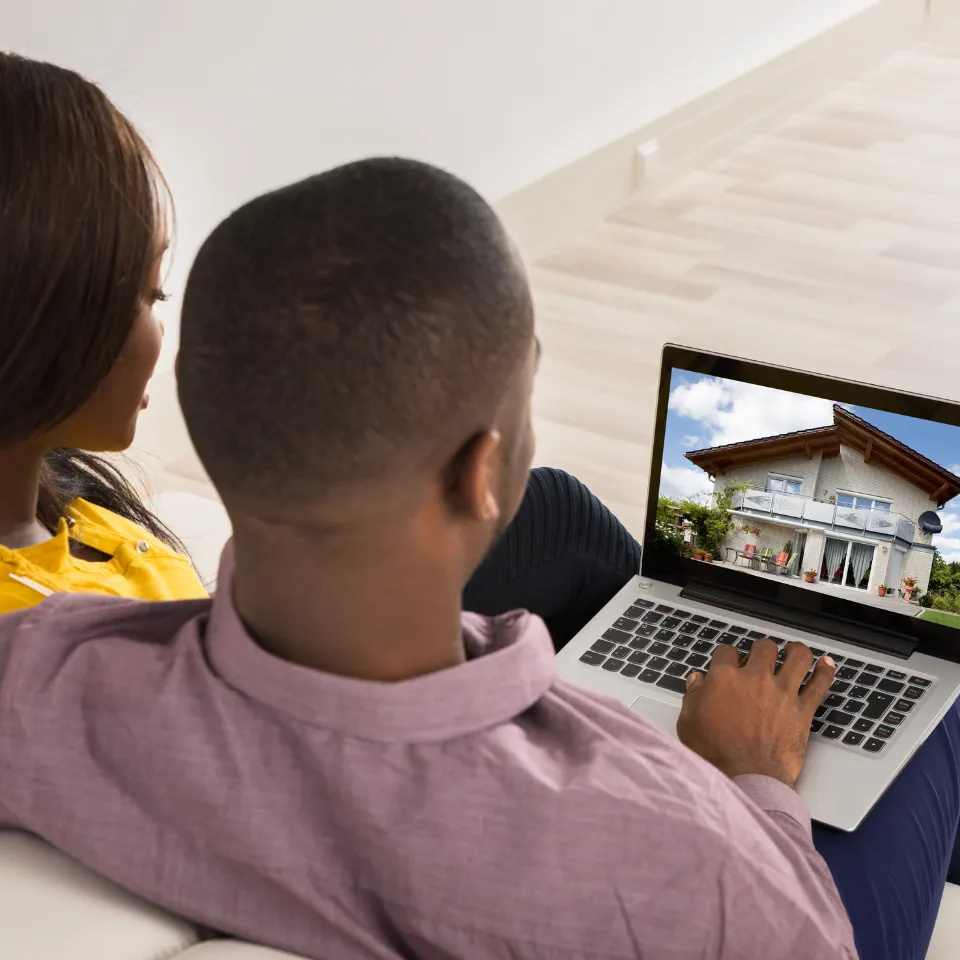 Worried couple reviewing housing market data on a laptop with paperwork on the table.
