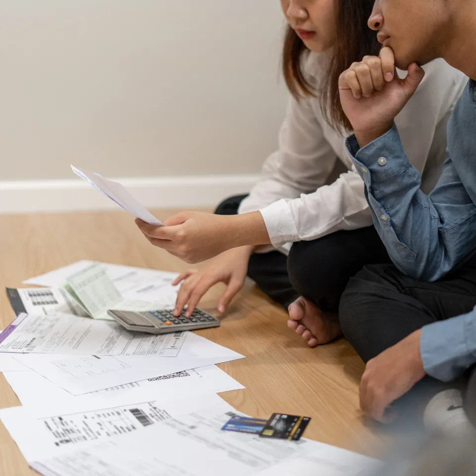 Worried couple reviewing home price data and market trends on a laptop at home with financial documents spread out on the table.