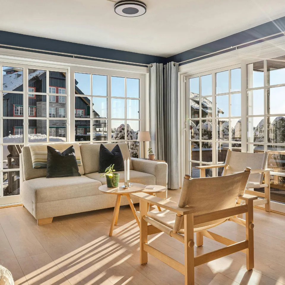 Bright living room with large windows, sheer curtains, mirrors, and light-colored decor.