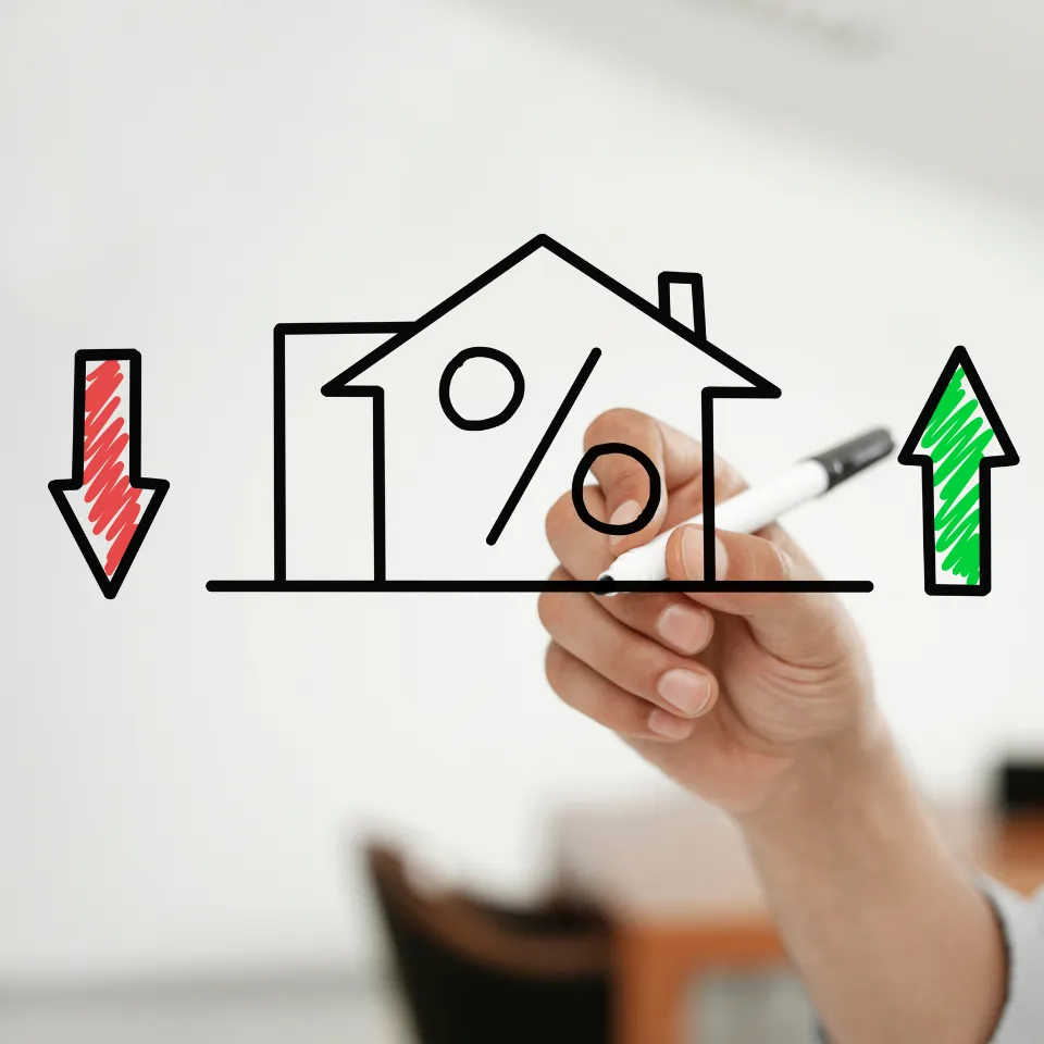 A house with a “For Sale” sign next to falling mortgage rate graphics, symbolizing the Fed’s rate cuts impacting the housing market.