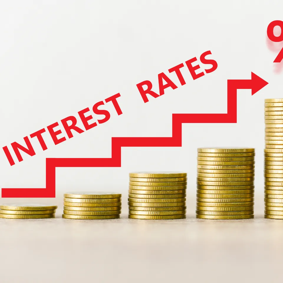 Stack of coins, small house model, and rising interest rate chart.