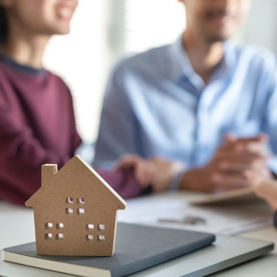 Couple reviewing listings with real estate agent in bright, sunny living room.