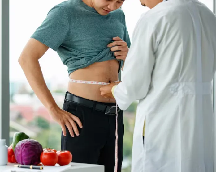 man in medical uniform measuring waist of crop male patient during work in clinic