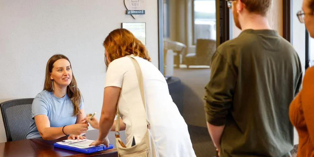 A line of people at a desk where a woman sits to represent church activity sign-ups.