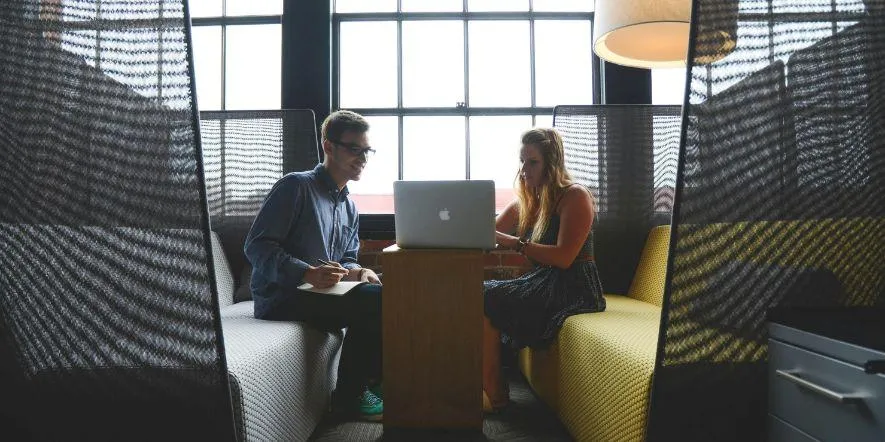 Male and female team members sitting on modern benches and looking at laptop. 