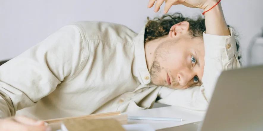 Man in a button-down shirt resting his head on his arm and staring at a laptop showing an example of church staff burnout.