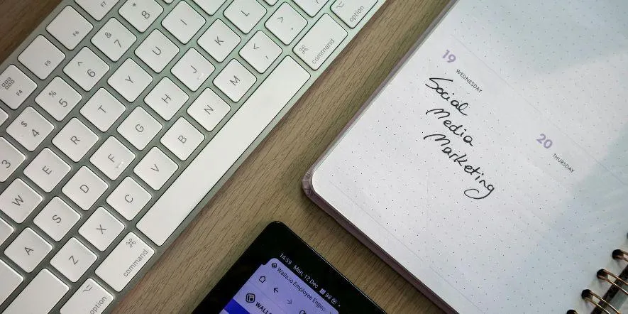 Planner open to an entry that reads social media marketing next to a keyboard and tablet.