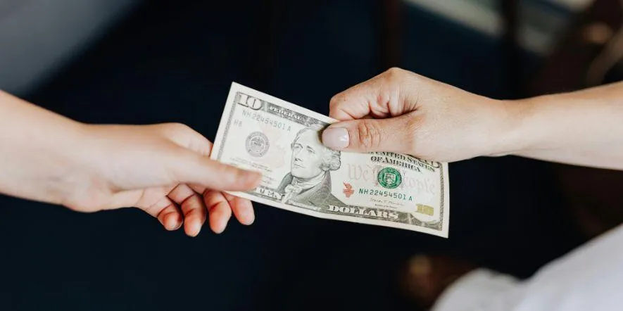 Two hands exchanging a $10 bill to represent church giving. 
