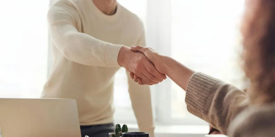 A man and a woman shaking hands over a desk during a meeting for hiring church staff.