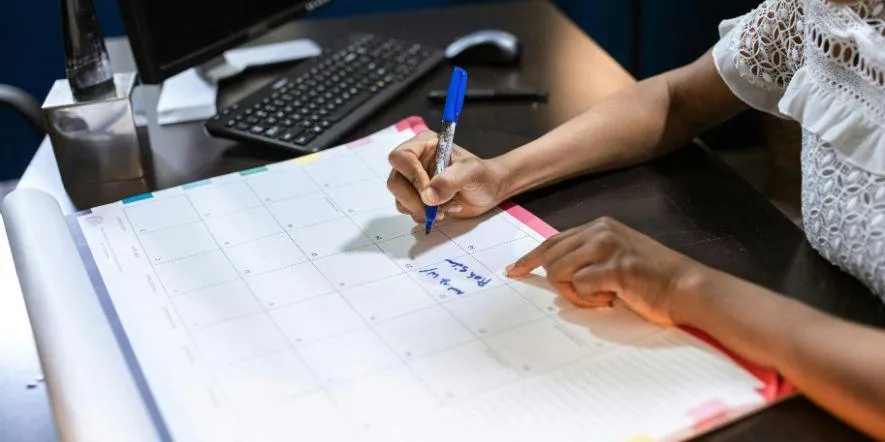 A church administrator writing on a calendar mat at her desk, jotting down blog topics for June.