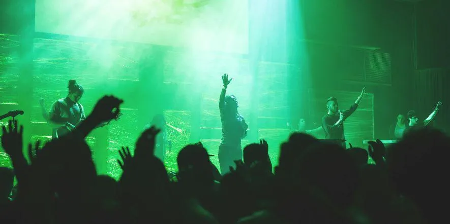 A church worship group playing music under a spotlight as the audience follows along with the lyrics on a projector.