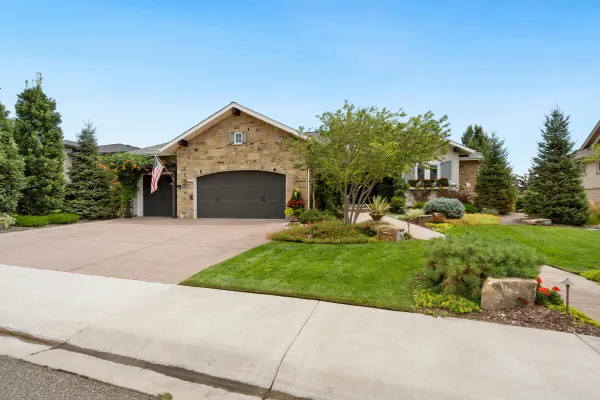 Single-story stone house with a wide concrete driveway and manicured front lawn.