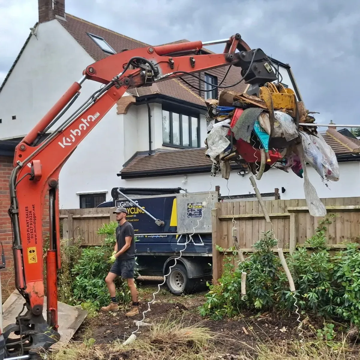 Mini excavator lifting mixed garden debris during site clearance