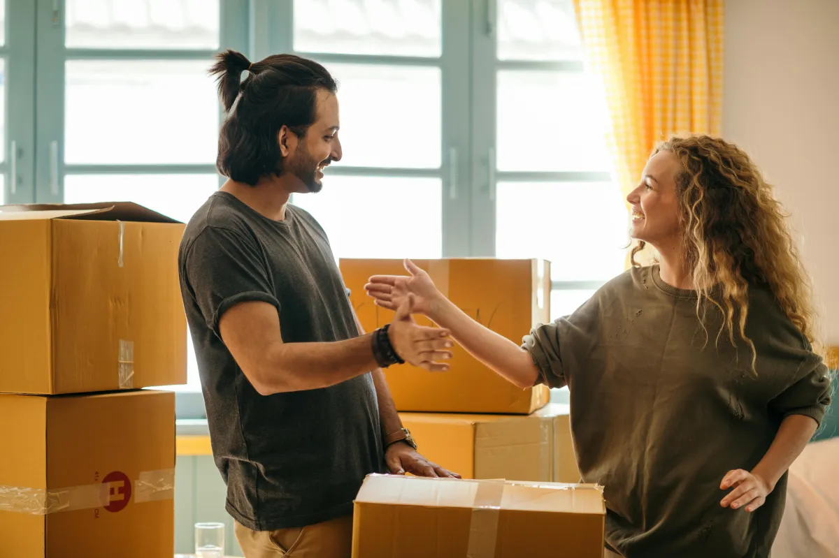 Couple laughing while unpacking boxes in a sunlit new home.