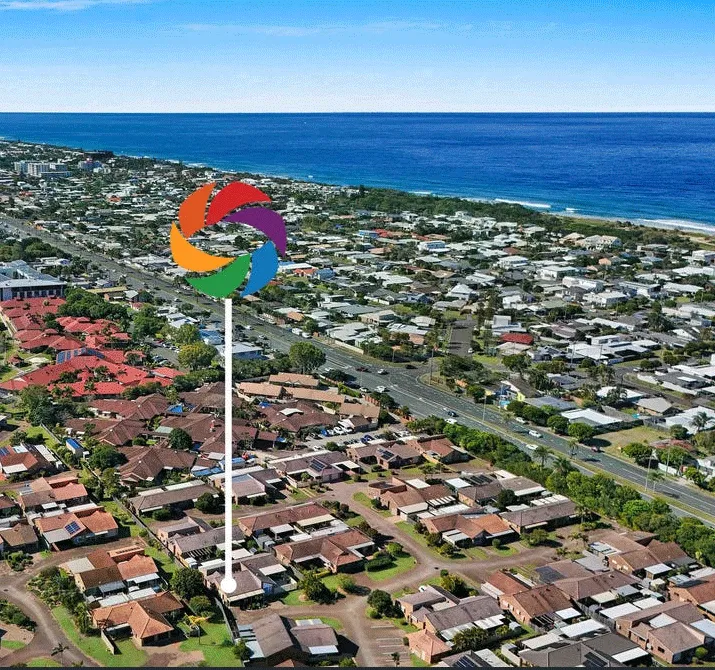 Aerial view of coastal suburb with modern homes stretching toward the ocean under blue skies.