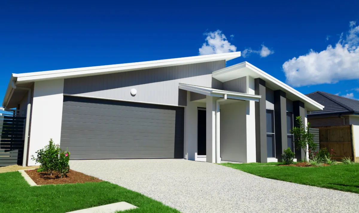 Suburban Sunshine Coast street lined with houses, trees, and lawns under blue sky, representing property costs and homeownership.