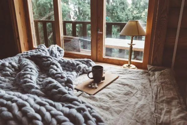 wooden home with a balcony. Cosy bed with a grey blanket, and a coffee with a view to the cold outside.