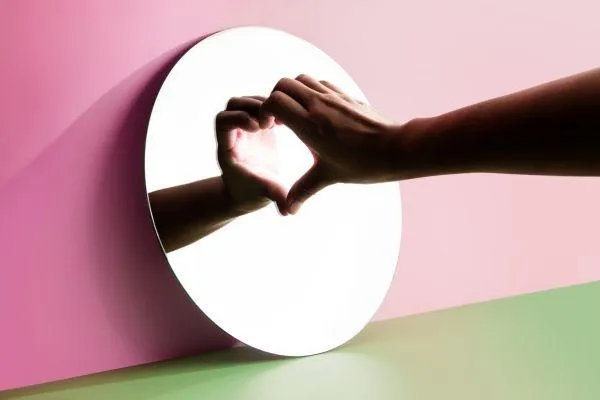 A mirror with someone making half a heart and the reflection making it a whole heart.