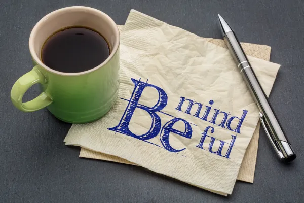 Coffee in mug, napkin with ‘be mindful’ printed on it, pen.