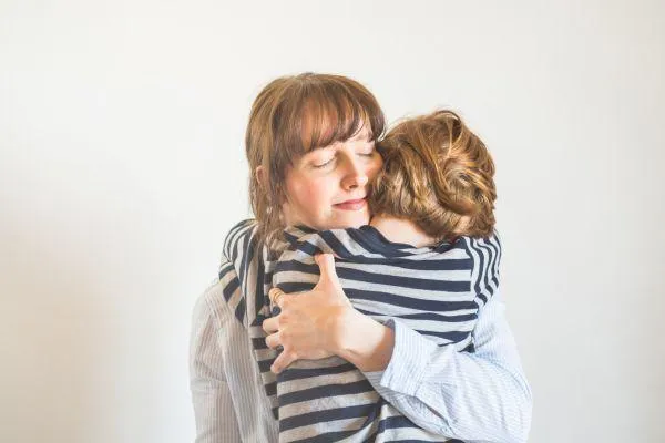 a mother cuddling her child. White background, with mother facing us and the child with his head over the mothers shoulder.