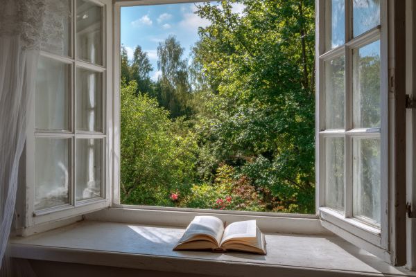 Open window with trees outside with a book on the windowsill.