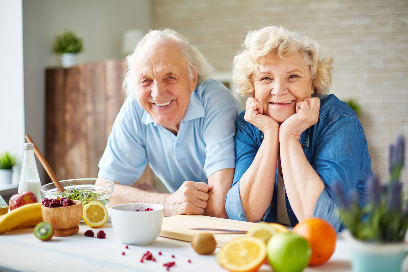 Couple de personnes âgées souriantes à table avec des fruits, symbole de vitalité et de mode de vie sain.